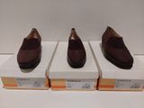trois paires de chaussures marron posées sur des cartons, sur une surface blanche