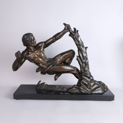 bronze statue of a man sitting on a tree branch with his hands in the air