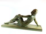 bronze statue of a woman laying on her stomach on a wooden base