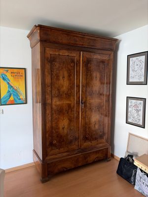une grande armoire en bois dans une pièce où sont accrochés des tableaux au mur