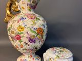 a white vase with a gold handle and a small stool