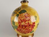 a yellow vase with red flowers on it on a white surface