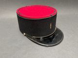 un chapeau haut-de-forme noir et rouge posé sur un socle noir, lui-même posé sur une surface grise