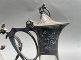 a silver pitcher sitting on top of a table next to a glass