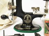 a black sewing machine with a green base next to a box and a pair of scissors