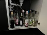many bottles of alcohol sitting on a shelf under a sink