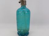 a blue glass bottle with a metal spout on a white surface