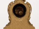 a gold clock on a table with a white wall in the background