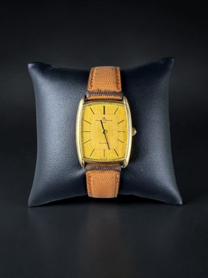 a close up of a watch on a pillow on a black surface