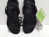 une paire de sandales noires posées sur une surface blanche, avec une étiquette de prix