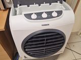 un petit climatiseur posé par terre à côté d'un micro-ondes