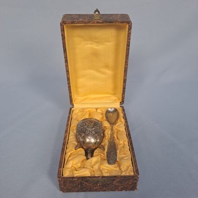 un petit objet en argent dans une boîte en bois, avec une cuillère et un repose-cuillère