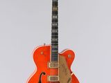une guitare électrique orange suspendue à une ficelle sur un mur blanc