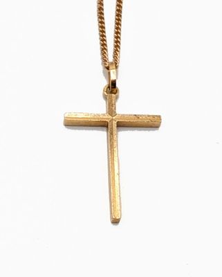 pendentif en forme de croix en or, suspendu à une chaîne en or, sur fond blanc