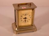 a small silver clock with a red cross on it