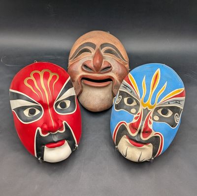 Trois masques de couleurs et de motifs différents sont posés sur une surface noire.