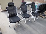 four black office chairs with white arms and wheels in a room