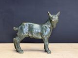 statue en bronze représentant une chèvre, posée sur une table en bois devant un mur noir