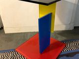 une table avec un plateau noir et un piètement rouge et bleu