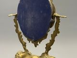 une image représentant un miroir ovale doré et bleu posé sur un pied