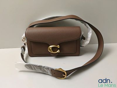 un petit sac à main marron orné d'une boucle dorée, posé sur une table blanche