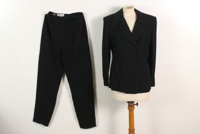 un costume noir et un pantalon posés sur un support à côté d'un mannequin