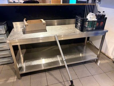 une table de travail en acier inoxydable sur laquelle est posé un bac contenant de la nourriture