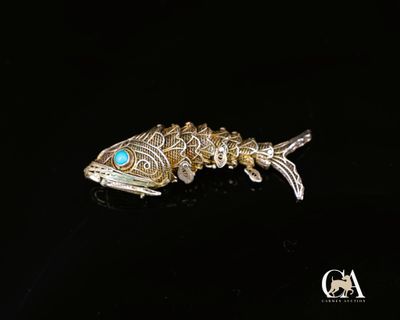 une broche en forme de poisson argenté aux yeux turquoise sur un fond noir