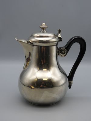 a silver coffee pot with a black handle on a grey surface