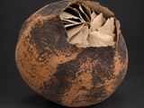 un vase marron contenant une feuille, sur fond noir