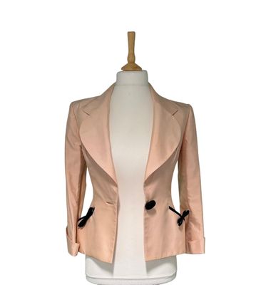 La veste est rose et comporte des boutons noirs sur le devant.