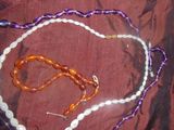 des colliers de perles violettes et blanches et un collier de perles violettes et blanches posé sur un tissu rouge