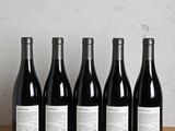 six bottles of red wine lined up on a wooden table