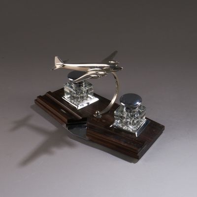 un avion argenté posé sur un socle en bois, surmonté d'une boule en verre