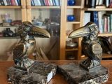 une paire d'oiseaux en bronze servant de serre-livres, posés sur une table en bois devant une bibliothèque