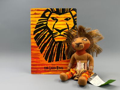 peluche assise à côté d'un livre sur lequel figure un lion