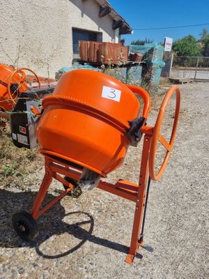 an orange cement mixer sitting in front of a building on a dirt road
