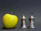 two pepper shakers next to an apple on a table