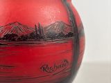 a red vase with a picture of a mountain range on it