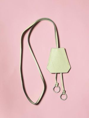 a white purse with a green strap on a pink background