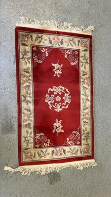 tapis accroché au mur d'une pièce où se trouve un tapis rouge et blanc