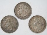three silver coins of different sizes and shapes on a white surface