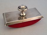 un petit objet métallique avec une base rouge sur une surface blanche