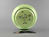 a green alarm clock with a sad face on it