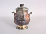 a silver and brown vase with a lid on a table