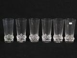 six clear glass shot glasses lined up against a black background