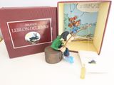 une figurine représentant une petite fille assise sur une souche d'arbre, avec un livre devant elle