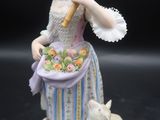 une figurine représentant une femme avec un panier de fleurs et un chat
