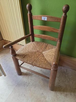 une chaise en bois avec une assise tressée, placée devant un mur vert