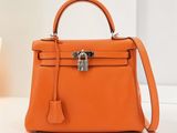 un petit sac Hermès orange posé sur une table, à côté d'une plante en pot
